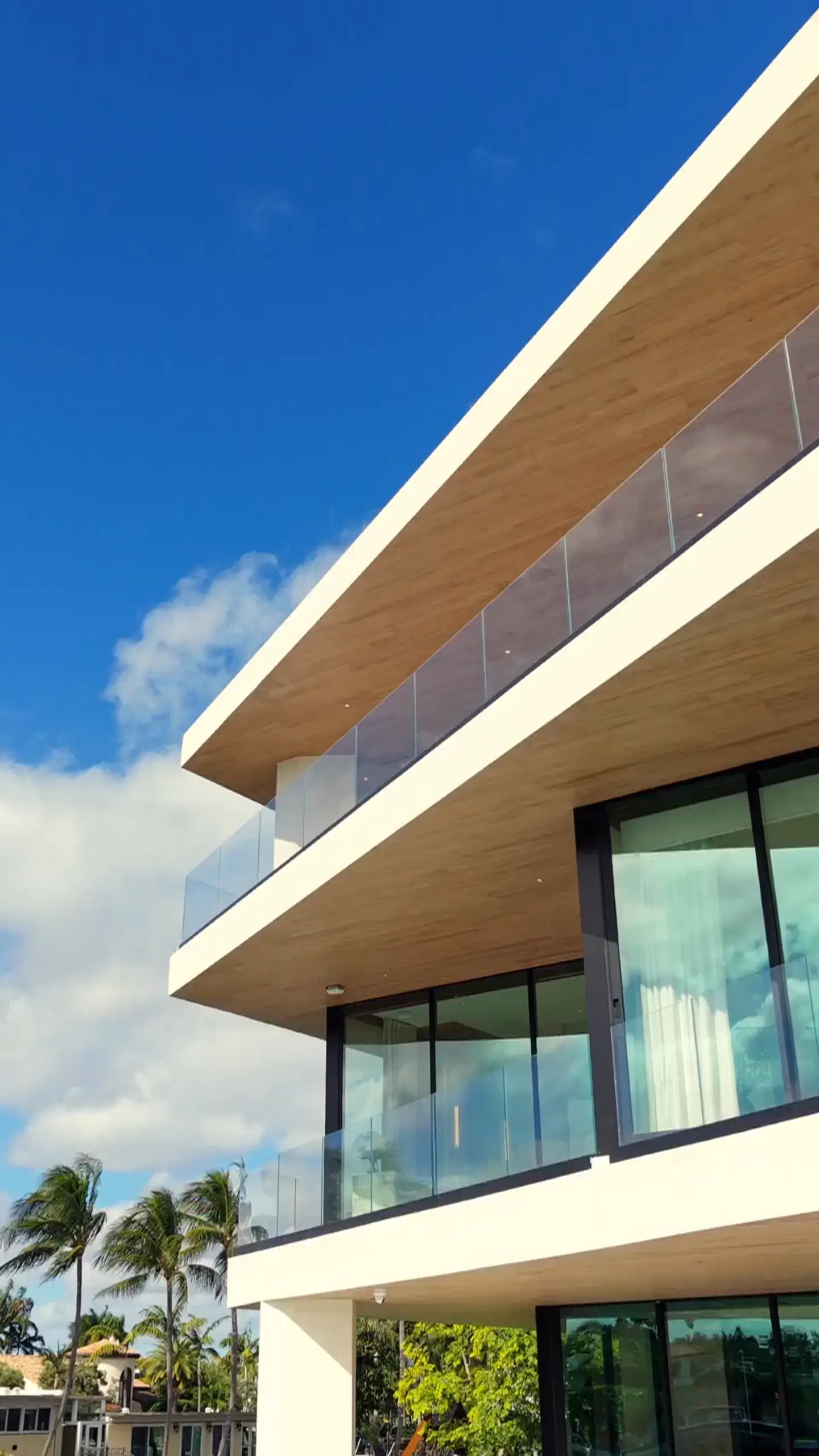 Modern white home with glass balconies and wood-lined overhangs under a blue South Florida sky